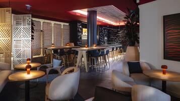 A modern bar area with round tables, bar stools, and a high ceiling with exposed beams.