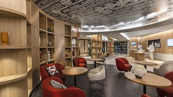 Un interior moderno con estanterías de madera curvada, sillas rojas y blancas, y mesas redondas.