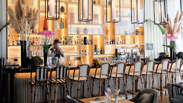 A bar area with wicker chairs, a bartender, and shelves stocked with bottles.