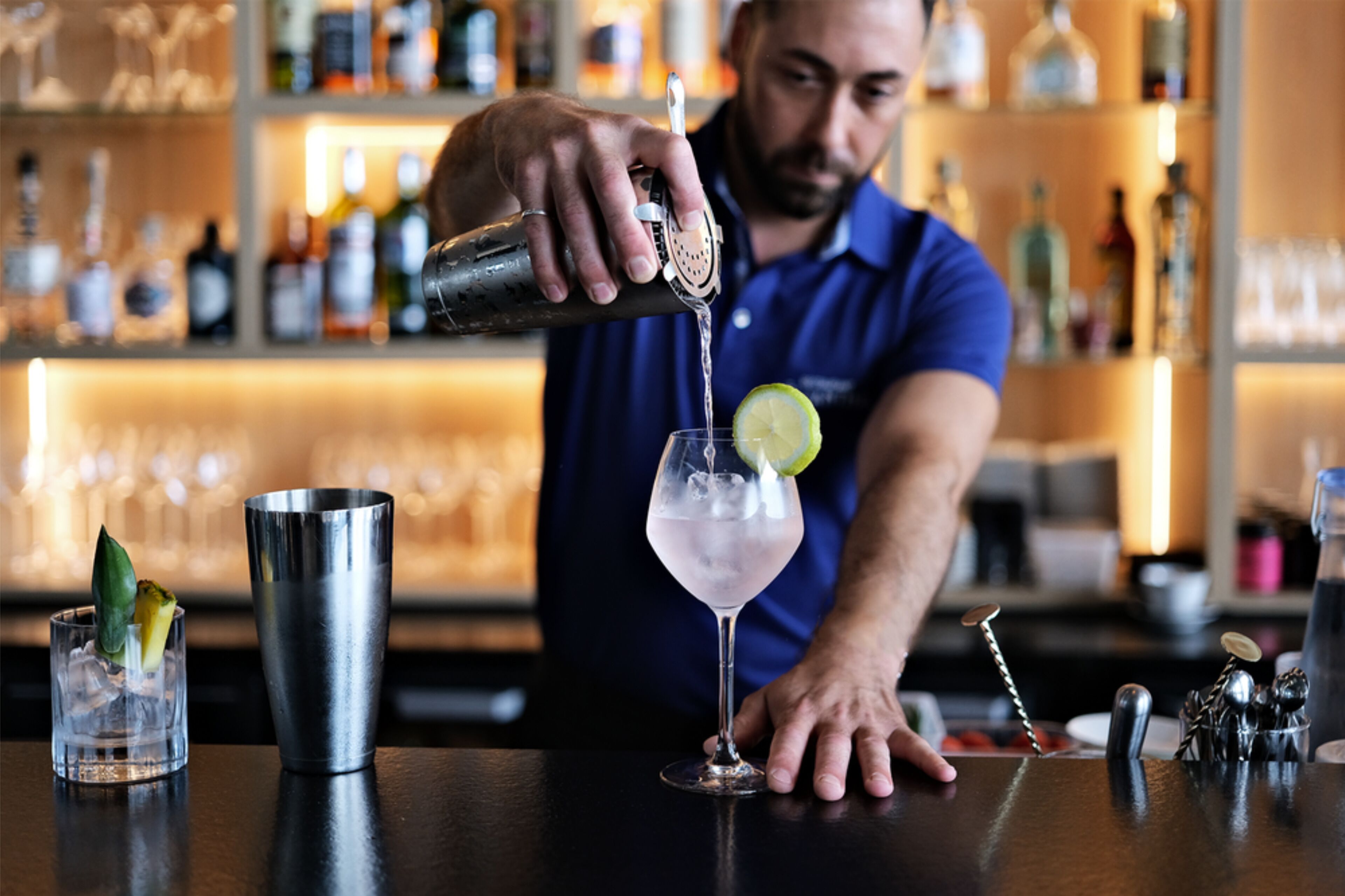 Un bartender vertiendo una bebida en un vaso con una rodaja de limón.