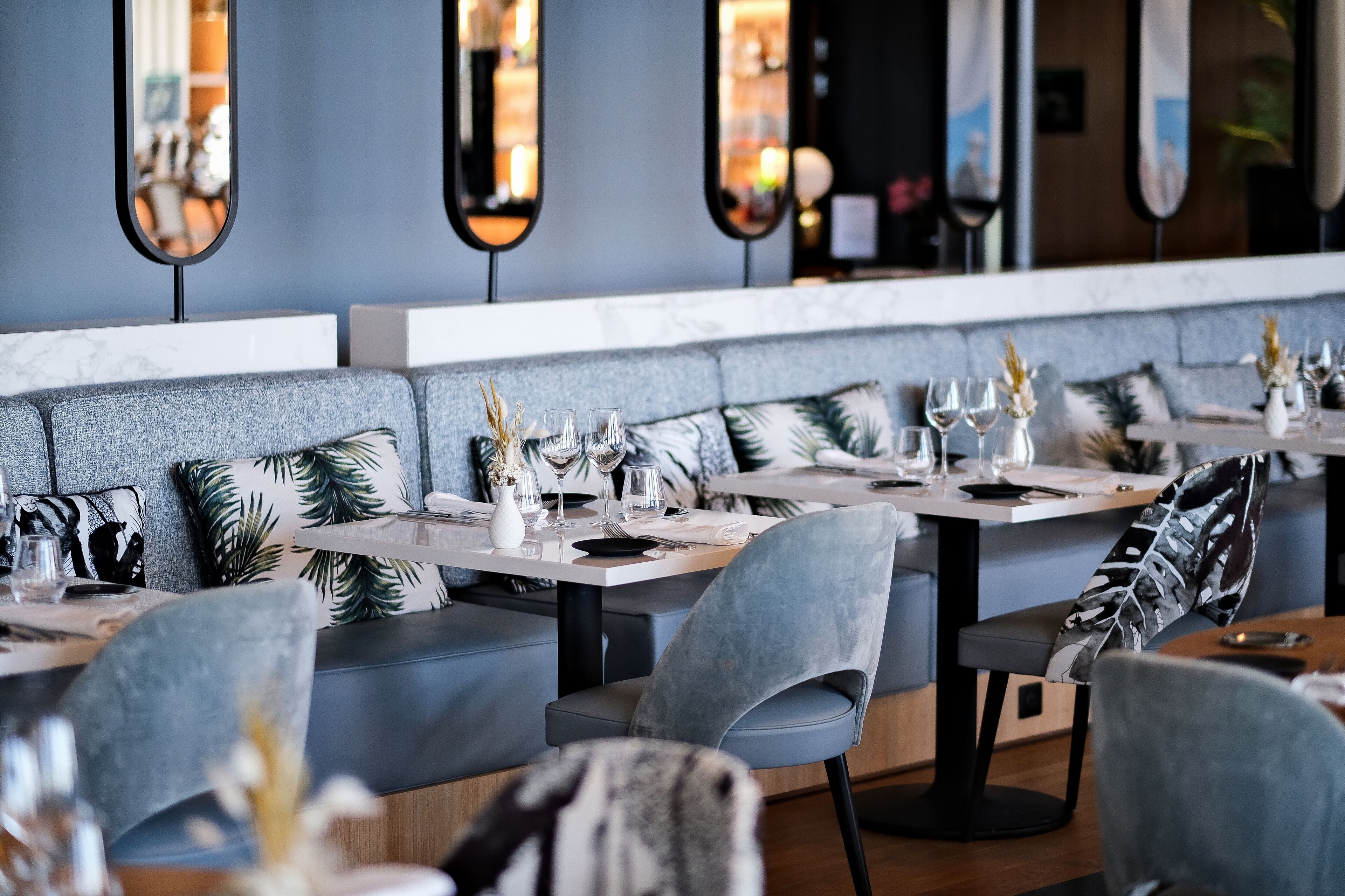 En modern restaurang med grå klädda sittplatser, vita bord och dekorativa vaser.