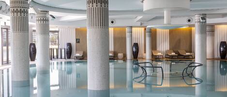 A large indoor swimming pool with modern architecture, including tall pillars and a clear glass floor.