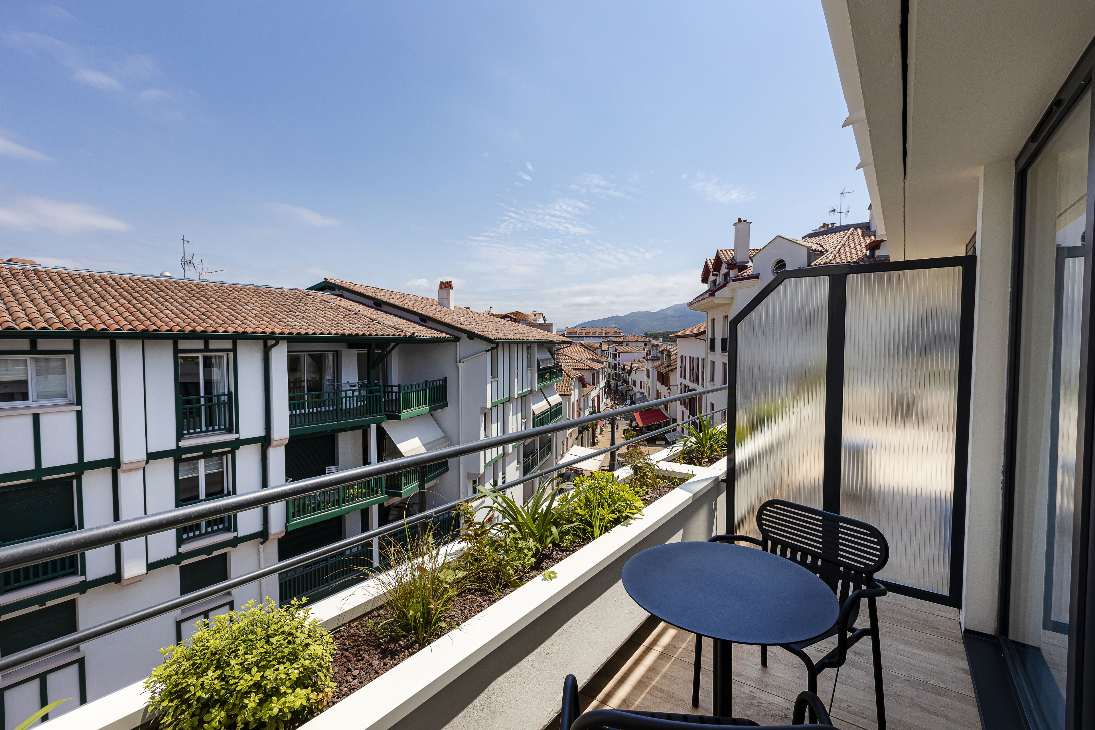 Een balkon met een tafel en stoelen, met uitzicht op een woongebied met terracotta dakpannen en balkons.