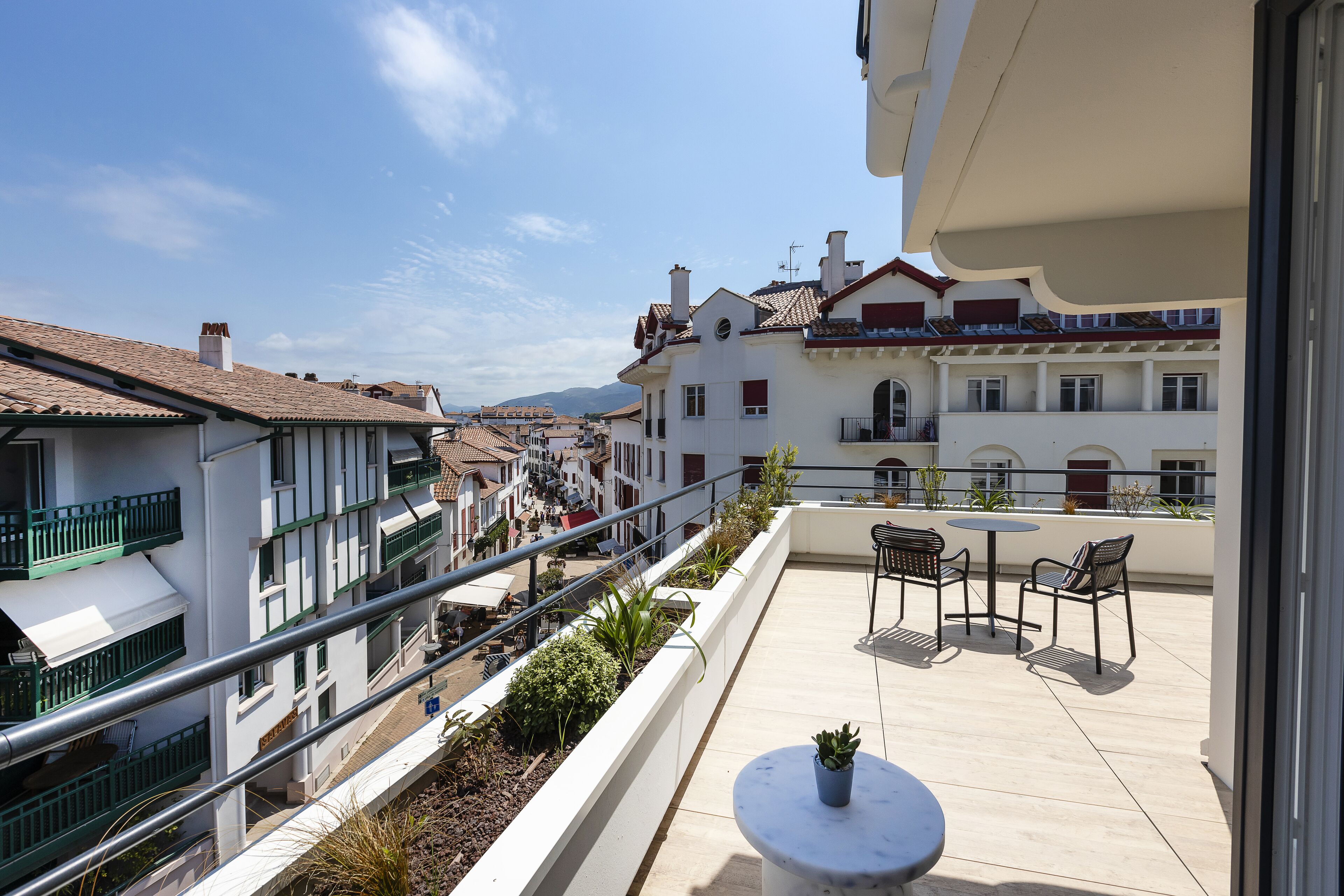 A rooftop terrace with outdoor seating, railings, and a view of the cityscape.