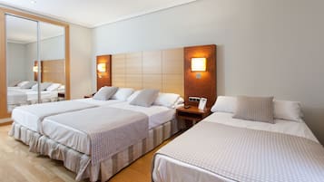 Habitación de hotel con tres camas, un espejo grande y un cabecero de madera con luces fijadas a la pared.