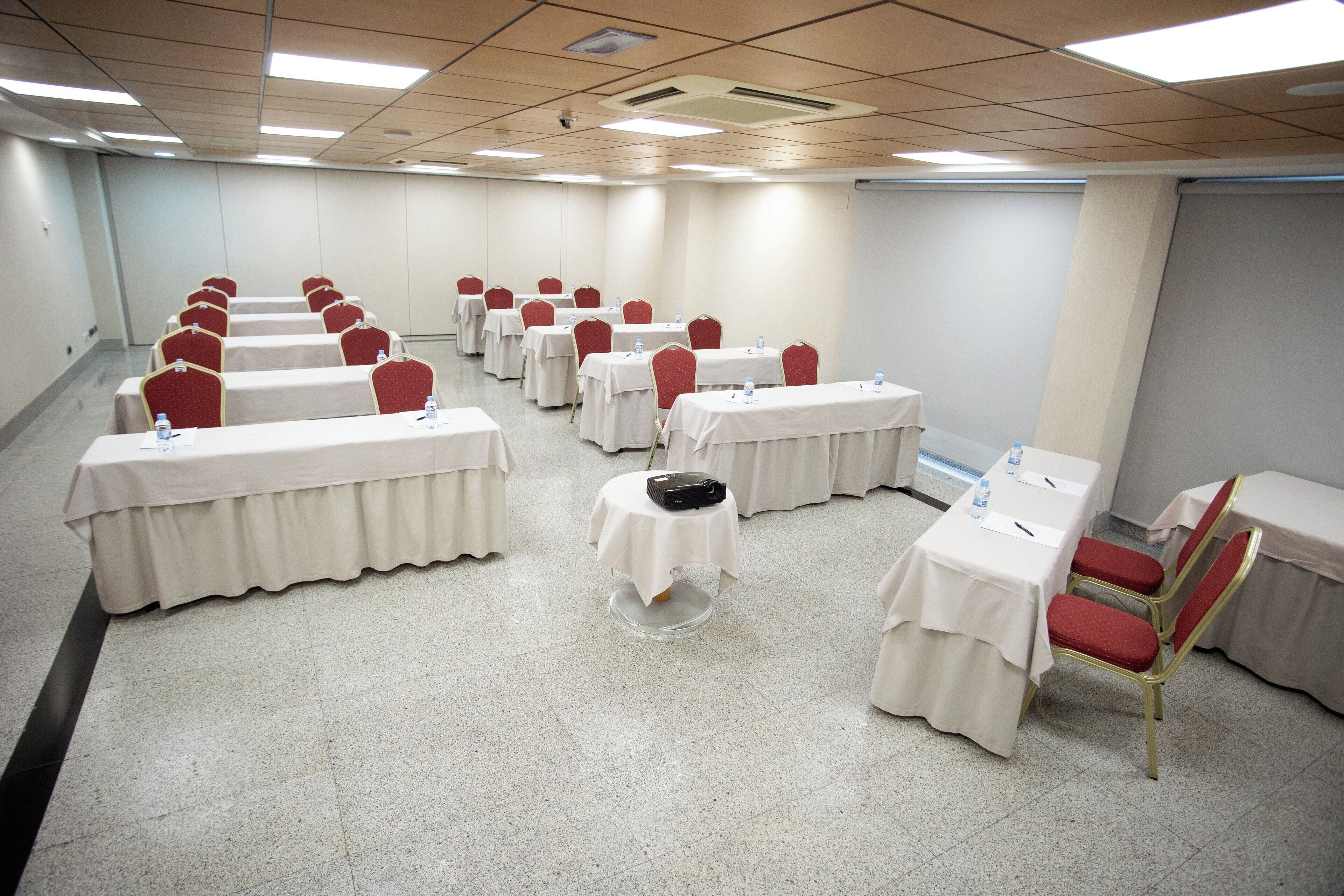 A conference room with multiple tables and chairs, equipped with water bottles and pens.