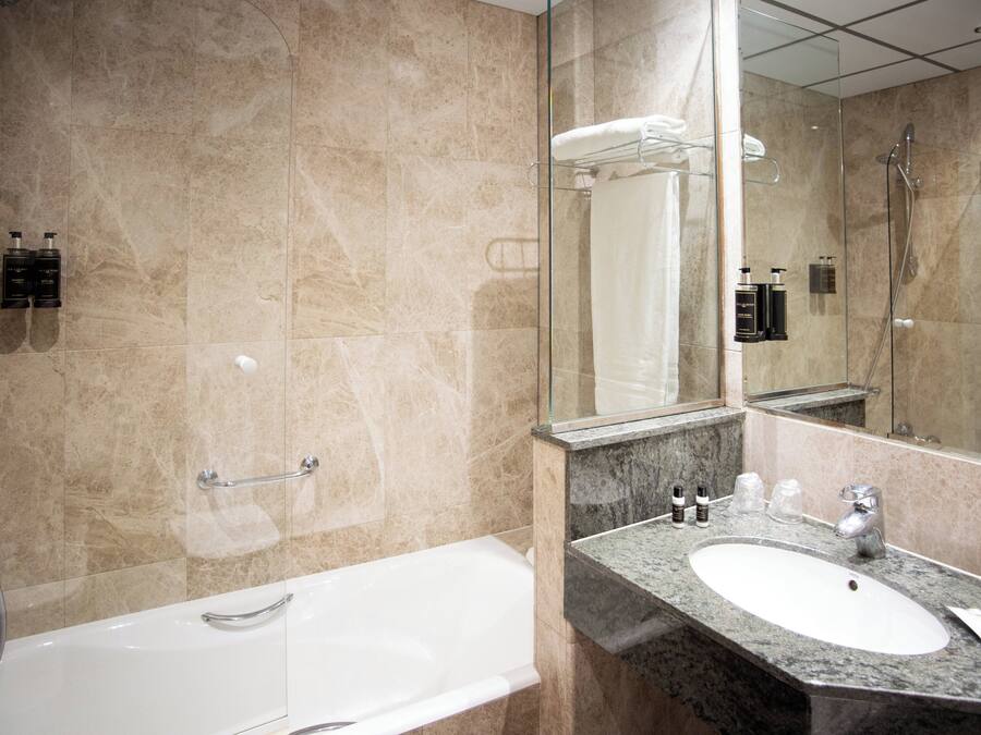 A modern bathroom with a large mirror, a bathtub, and a sink with toiletries.