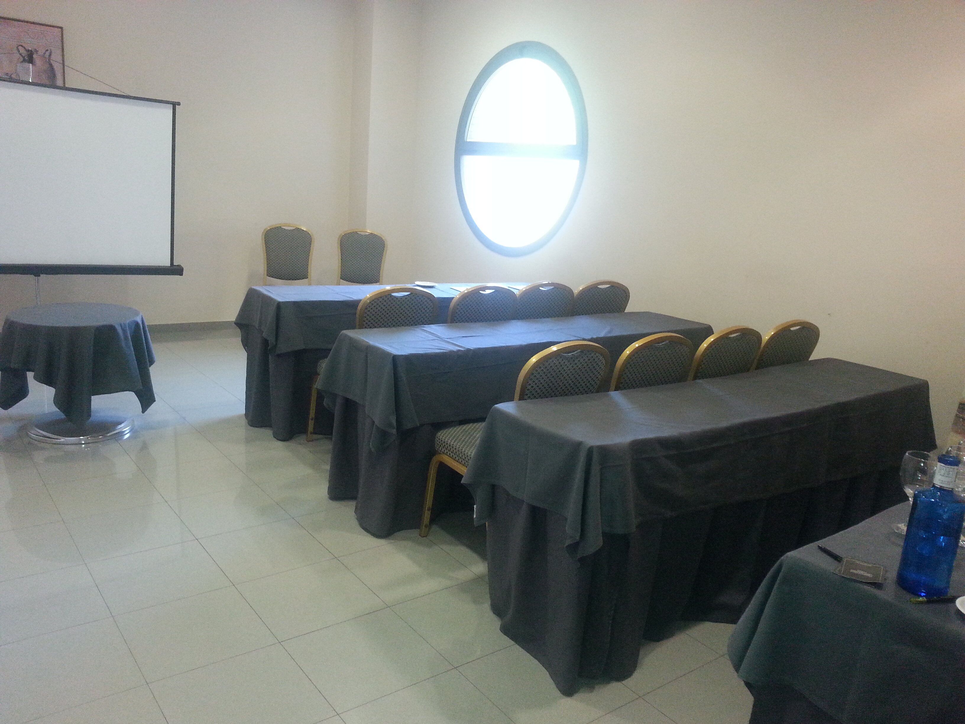 Une salle de conférence équipée de tables et de chaises, d’un écran de projection et d’une grande fenêtre.