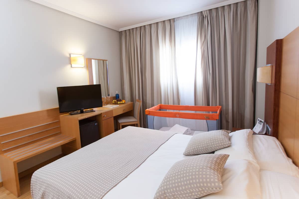 Ein Hotelzimmer mit einem Bett, einem Schreibtisch, einem Fernseher und einem fensterbepflanzten Fenster.