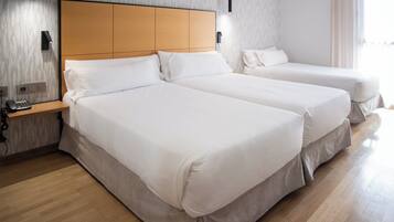 A hotel room with two beds, a wooden headboard, a bedside table with a phone, and a wall-mounted light fixture.