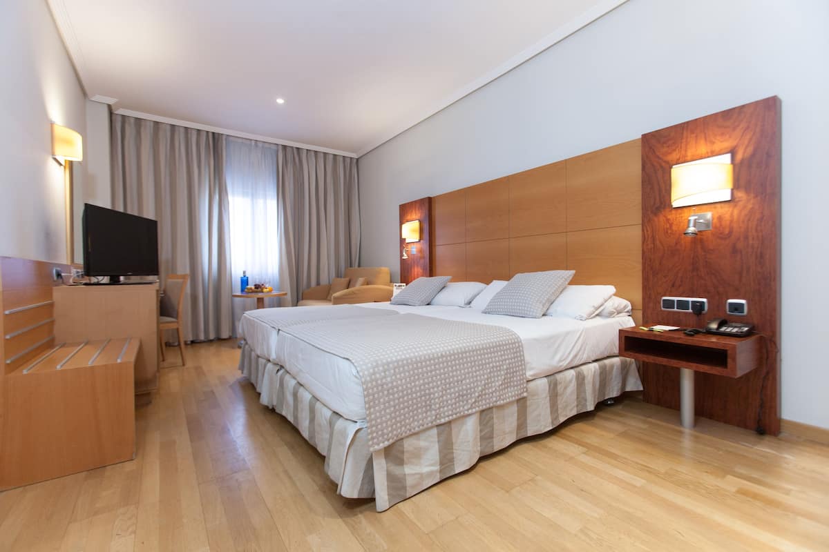 Ein Hotelzimmer mit einem großen Bett, einem Schreibtisch, einem Fernseher und einem Holzkopfende mit integrierter Beleuchtung.