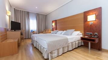 Een hotelkamer met een groot bed, een bureau, een televisie en een houten hoofdeinde met ingebouwde verlichting.