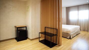 Une chambre d’hôtel avec un plancher en bois, un lit avec un matelas blanc, une table de chevet noire et une étagère noire.