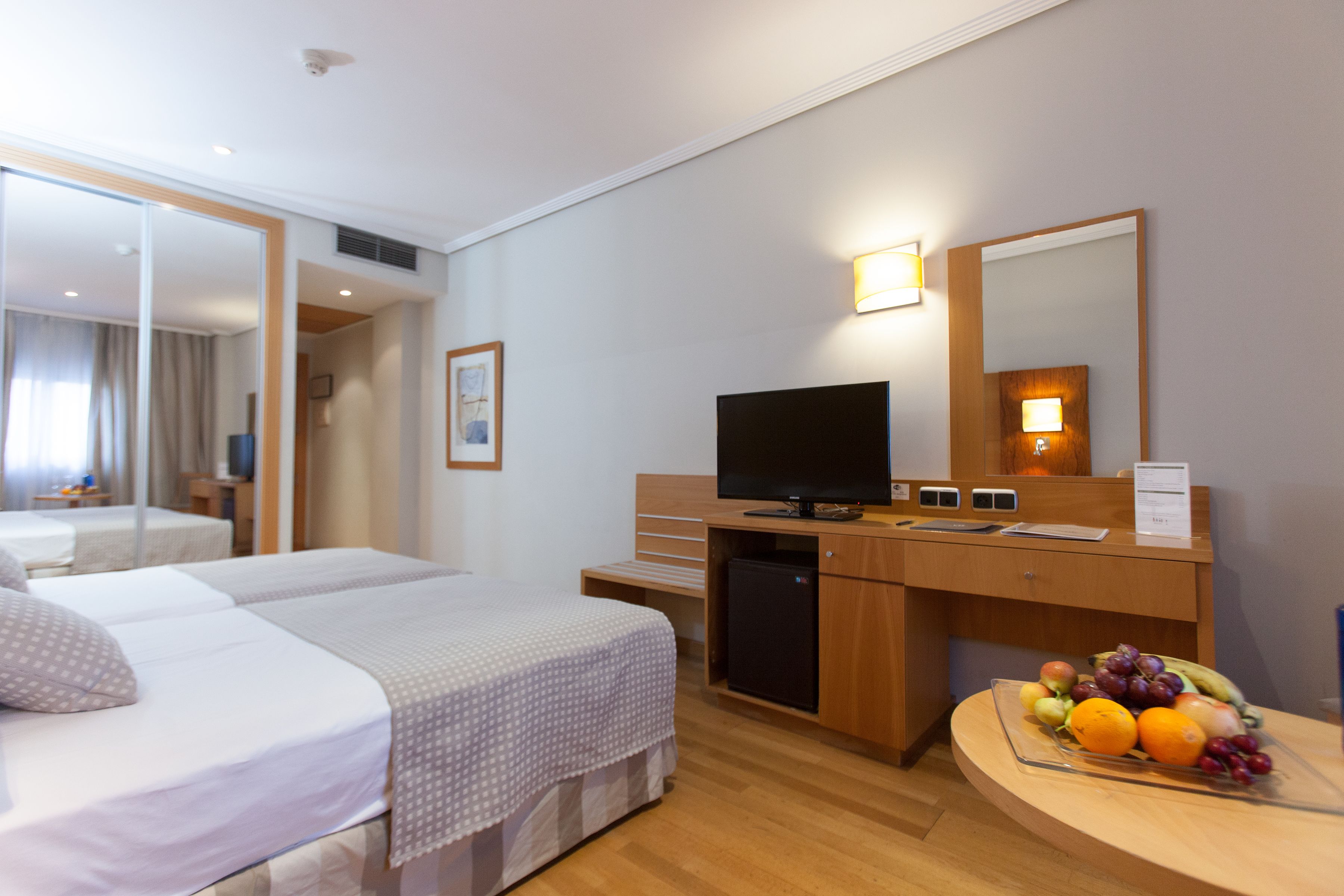 A hotel room with a bed, a desk with a computer, a television, and a fruit bowl.