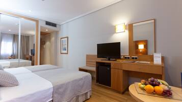 A hotel room with a bed, a desk with a computer, a television, and a fruit bowl.