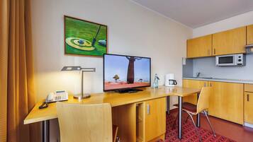 A compact hotel room with a desk, two chairs, a television, a microwave, and a small kitchenette.