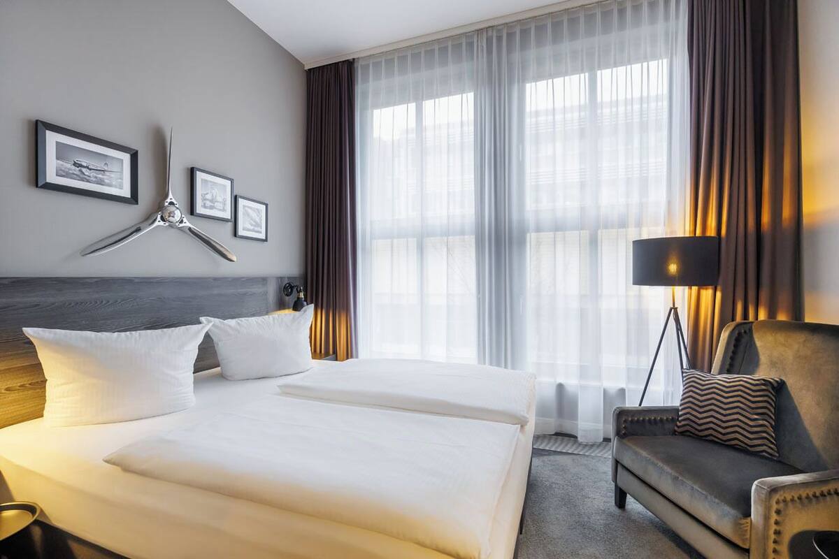 A hotel room with a large bed, a sofa, a desk, and a window with curtains.