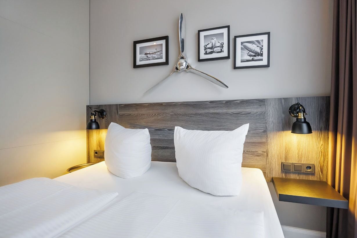 Una camera d'hotel con un letto grande, due comodini con lampade, una testiera in legno e tre quadri appesi alla parete.