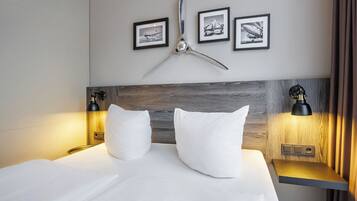 Una camera d'hotel con un letto grande, due comodini con lampade, una testiera in legno e tre quadri appesi alla parete.