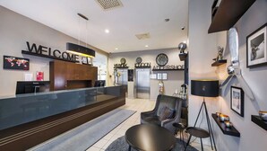 Un área de recepción moderna con mostrador, zona de estar con mesa redonda y pared decorada con relojes y cuadros.