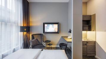 Ein Hotelzimmer mit Bett, Schreibtisch, Stuhl, kleinem Tisch, Fernseher und einer Küchenzeile.