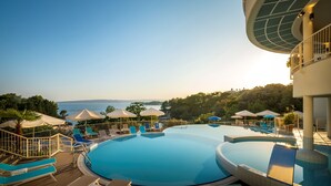 Un área de piscina en un resort con varias piscinas, tumbonas, sombrillas y vistas al mar.