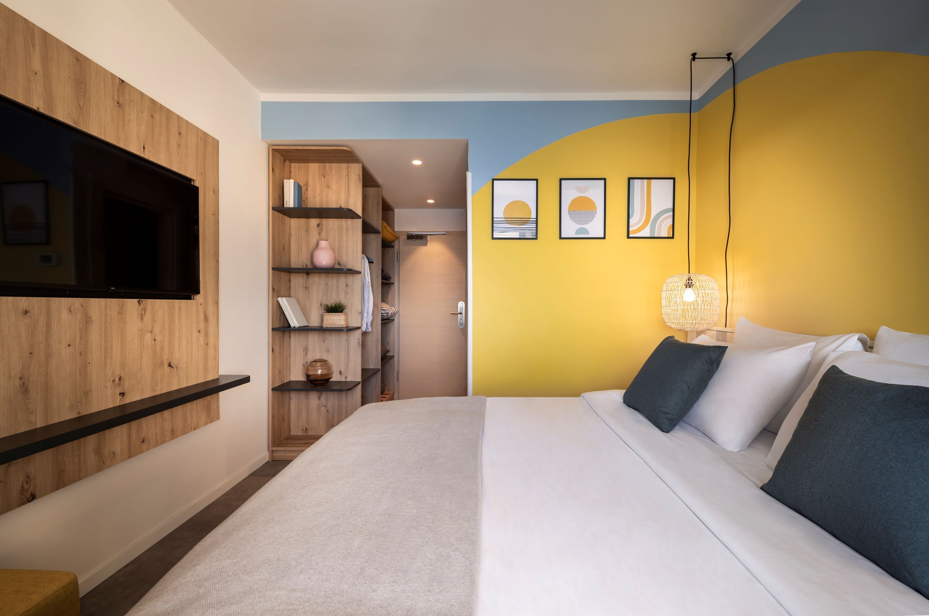 A modern bedroom with a bed, a TV mounted on a wooden wall, a wardrobe, and a bedside table.