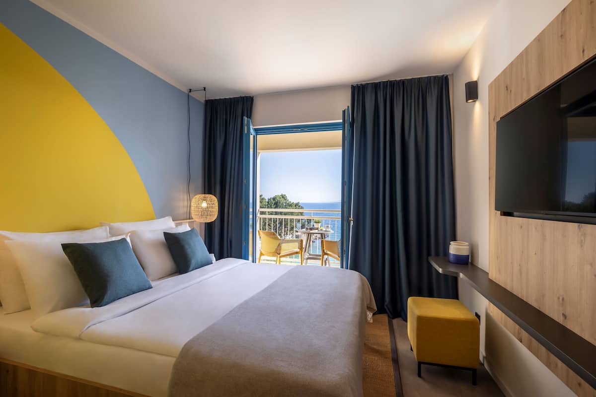 Een hotelkamer met een bed, een tafeltje, een stoel, een televisie en een balkon met uitzicht.