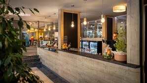 Zona de bar con mostrador de madera, lámparas colgantes y una vitrina refrigerada.