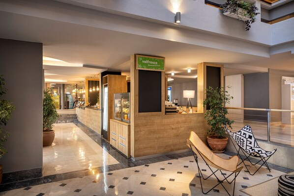 Un hall d’hôtel moderne avec un comptoir d’accueil, un espace salon et des plantes en pot.