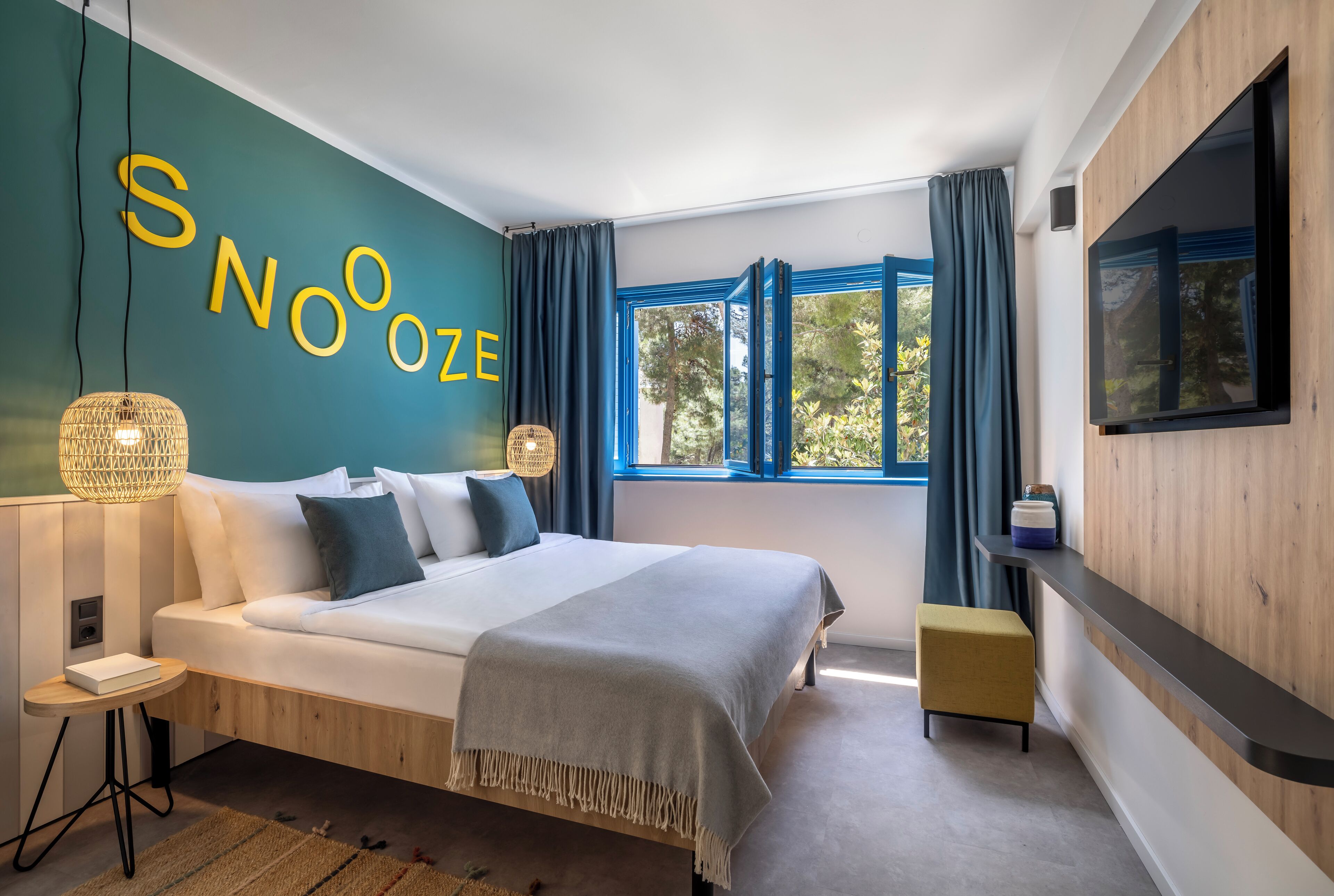 Een moderne slaapkamer met een groot bed, een aan de muur bevestigde televisie en een raam met gordijnen.