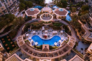 An aerial view of a resort with a central pool, multiple balconies, and lush landscaping.