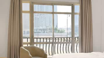 Habitación de hotel con un ventanal grande, una cama, una silla y vistas a un paisaje urbano.