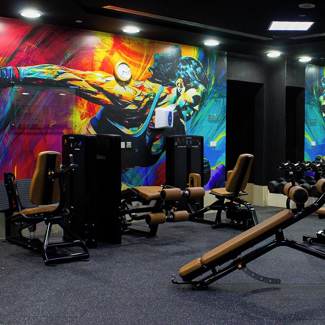 A gym with exercise equipment and a colorful mural on the wall.