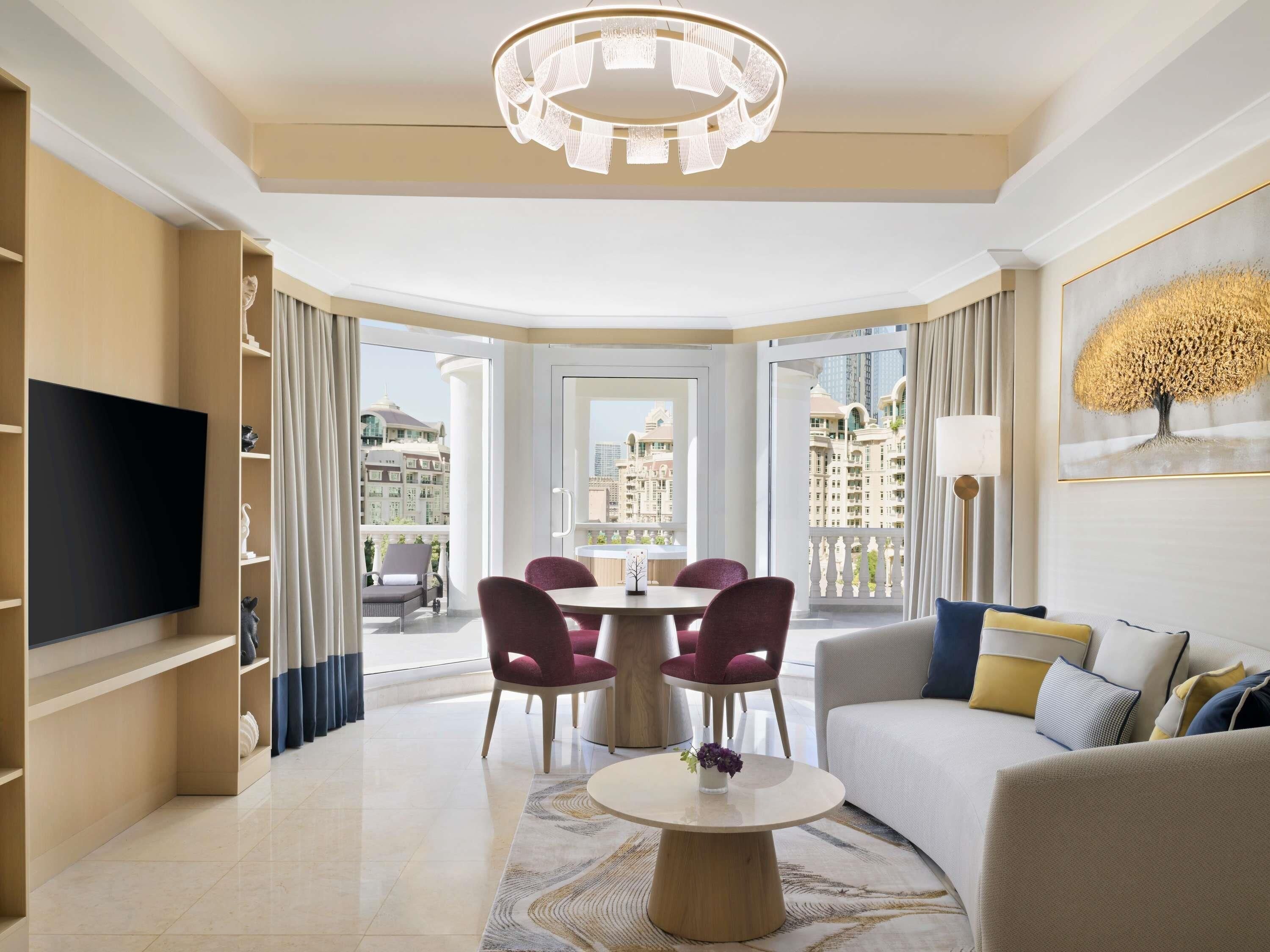 A modern living room with a flat-screen TV, a dining table with chairs, a sofa, and a chandelier.