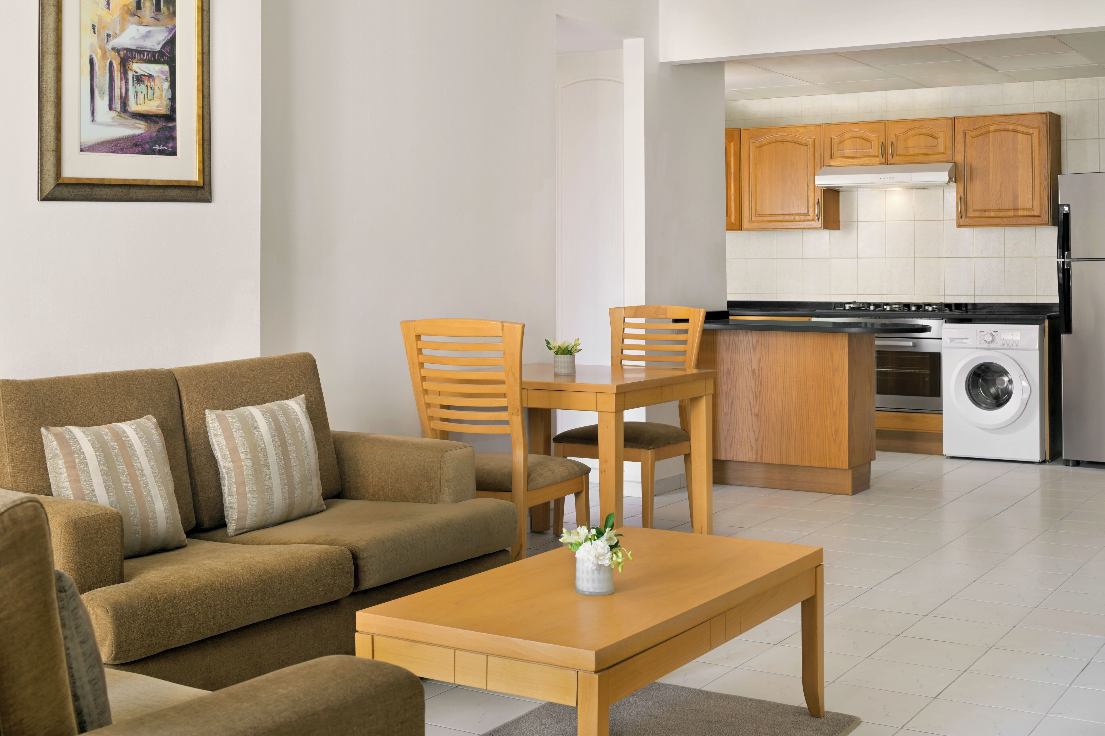 A living room with a sofa, chairs, a coffee table, and a kitchen area with wooden cabinets and appliances.