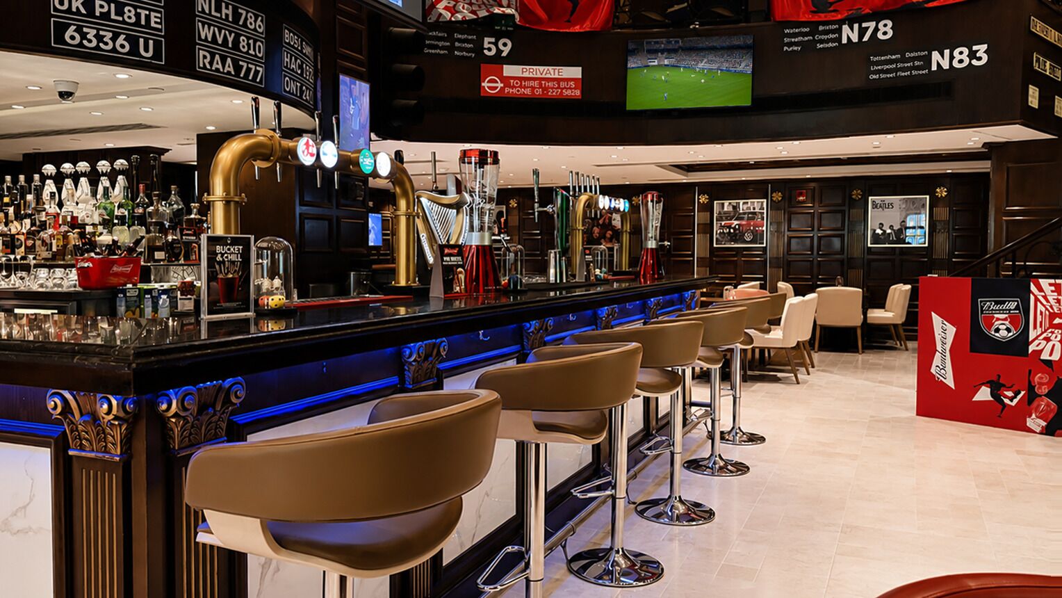 Un'area bar con sgabelli, un bancone e uno schermo televisivo che mostra un evento sportivo.