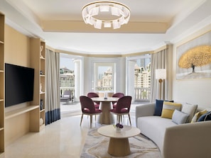 A modern living room with a flat-screen TV, a dining table with chairs, a sofa, and a chandelier.