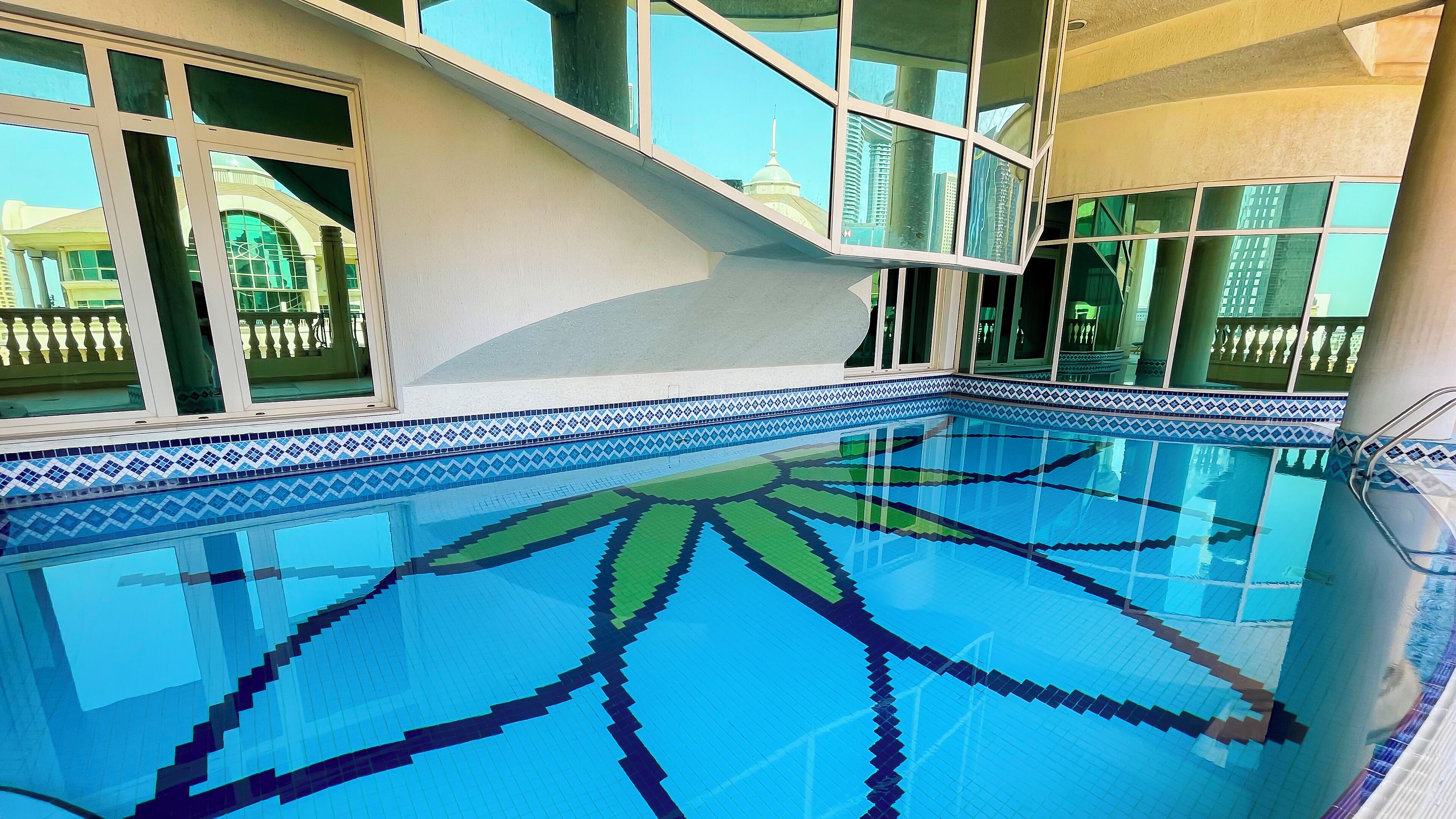 A swimming pool with a geometric tile pattern, large windows, and a view of a building with a dome.