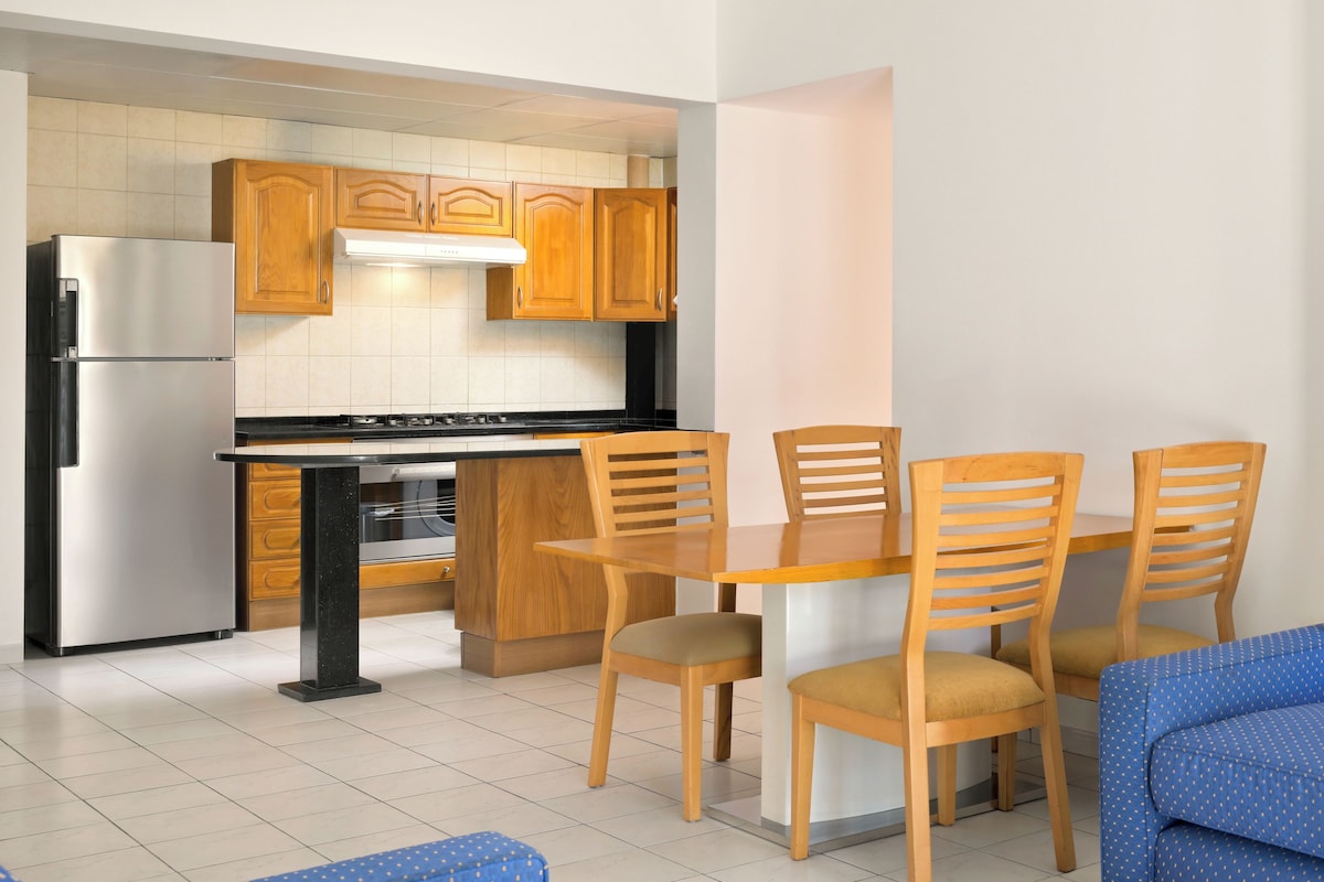 Une cuisine compacte avec des meubles en bois, un réfrigérateur en acier inoxydable, une table à manger avec des chaises et un canapé bleu.