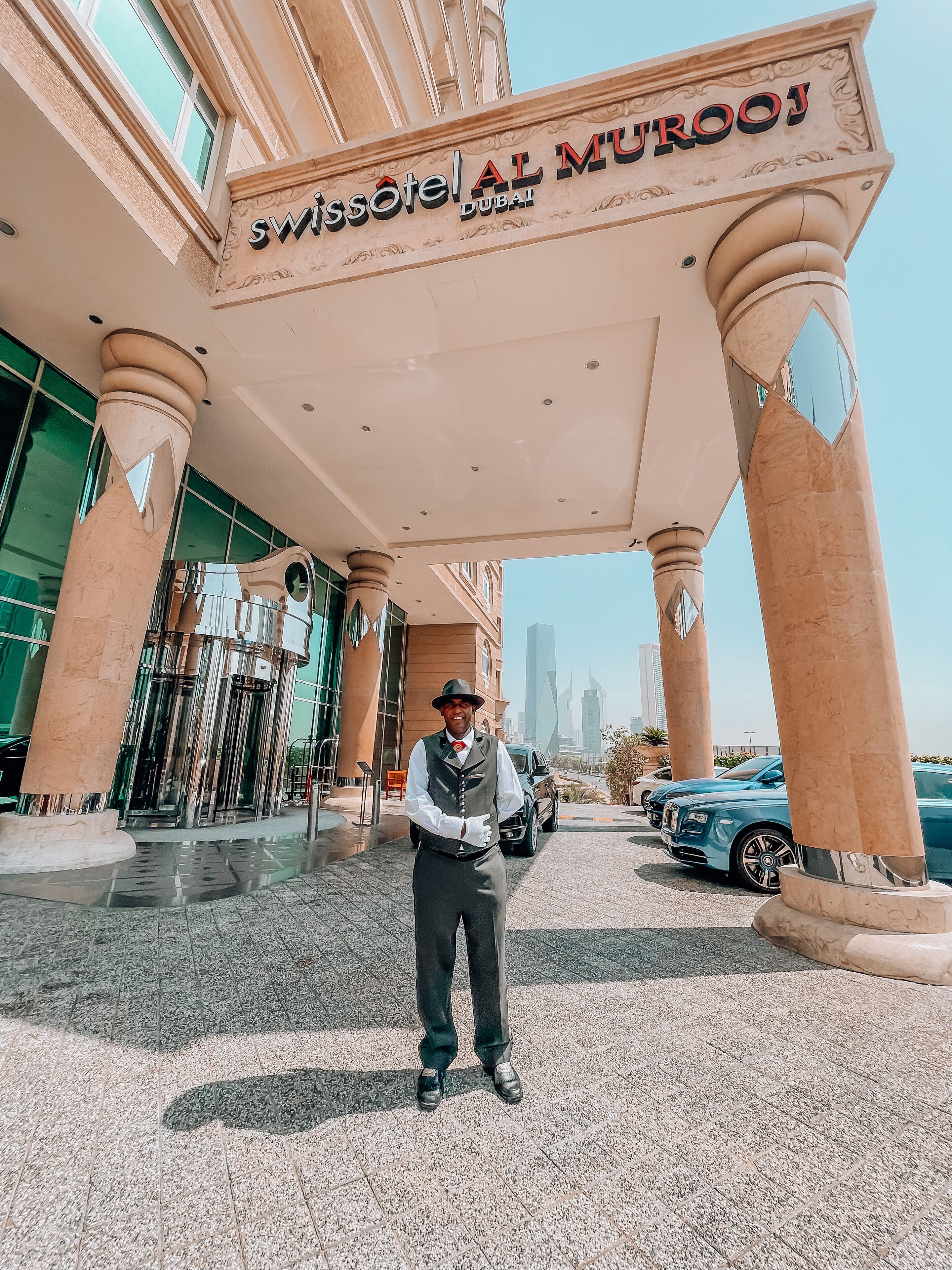 The entrance of the Swissotel Al Murooj in Dubai with a clear view of the city skyline in the background.