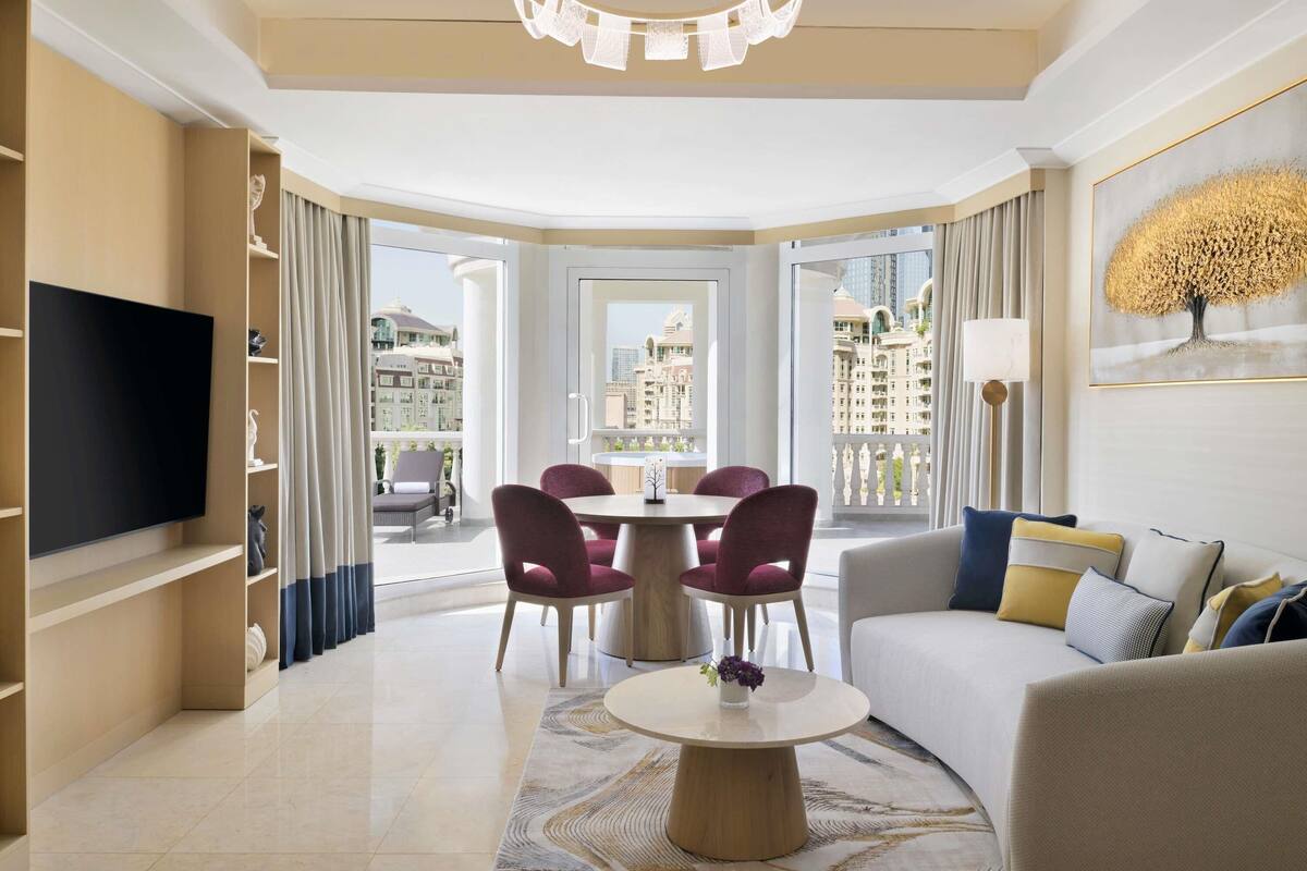 A modern living room with a flat-screen TV, a dining table with chairs, a sofa, and a chandelier.