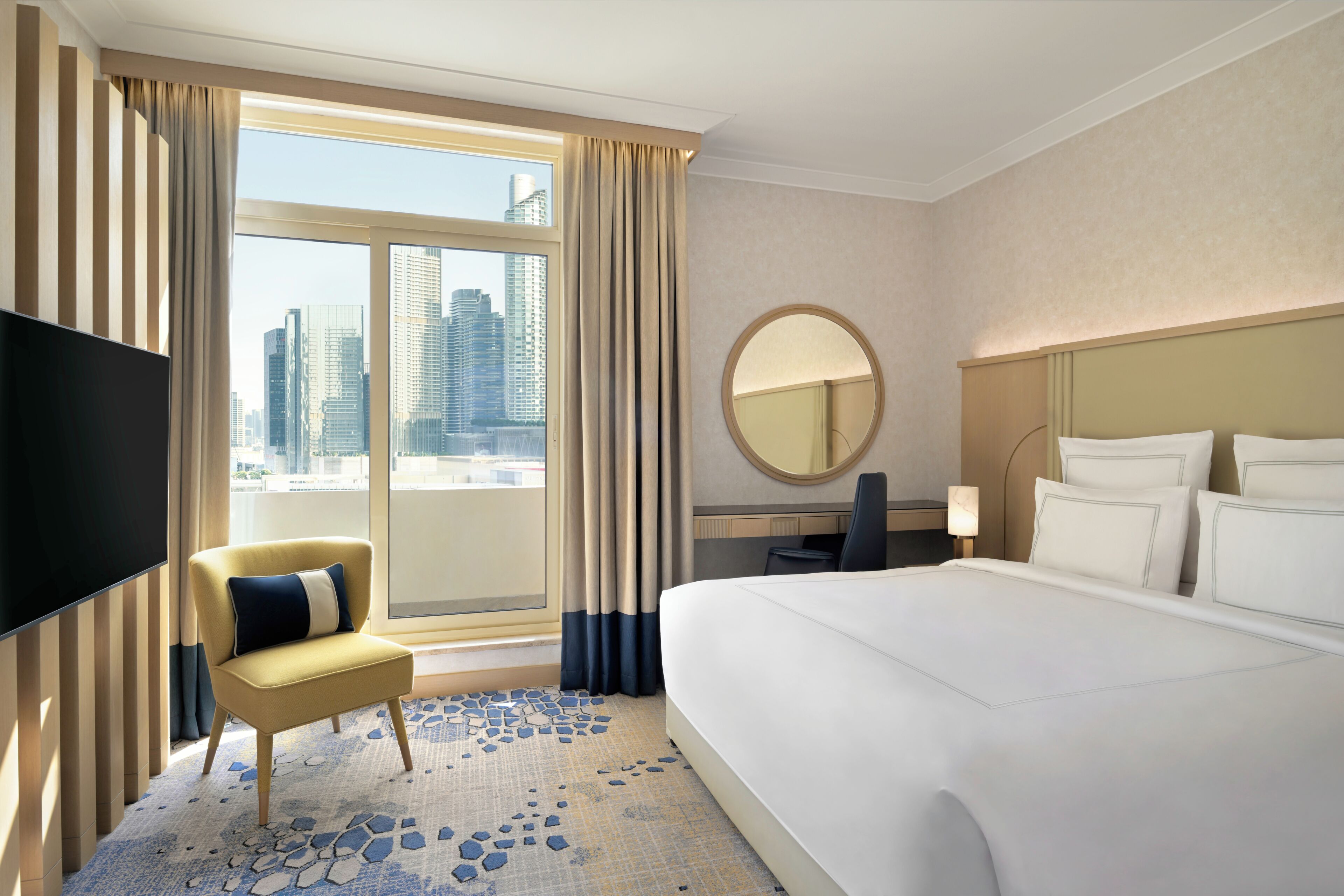 Quarto de hotel com uma cama grande, televisão, cadeira, escrivaninha e vista para a cidade.