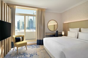 A hotel room with a large bed, a TV, a chair, a desk, and a view of the cityscape.