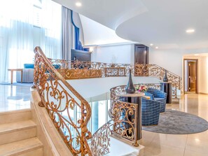 A spacious interior with a grand staircase, a modern kitchen, and a seating area with a blue sofa.