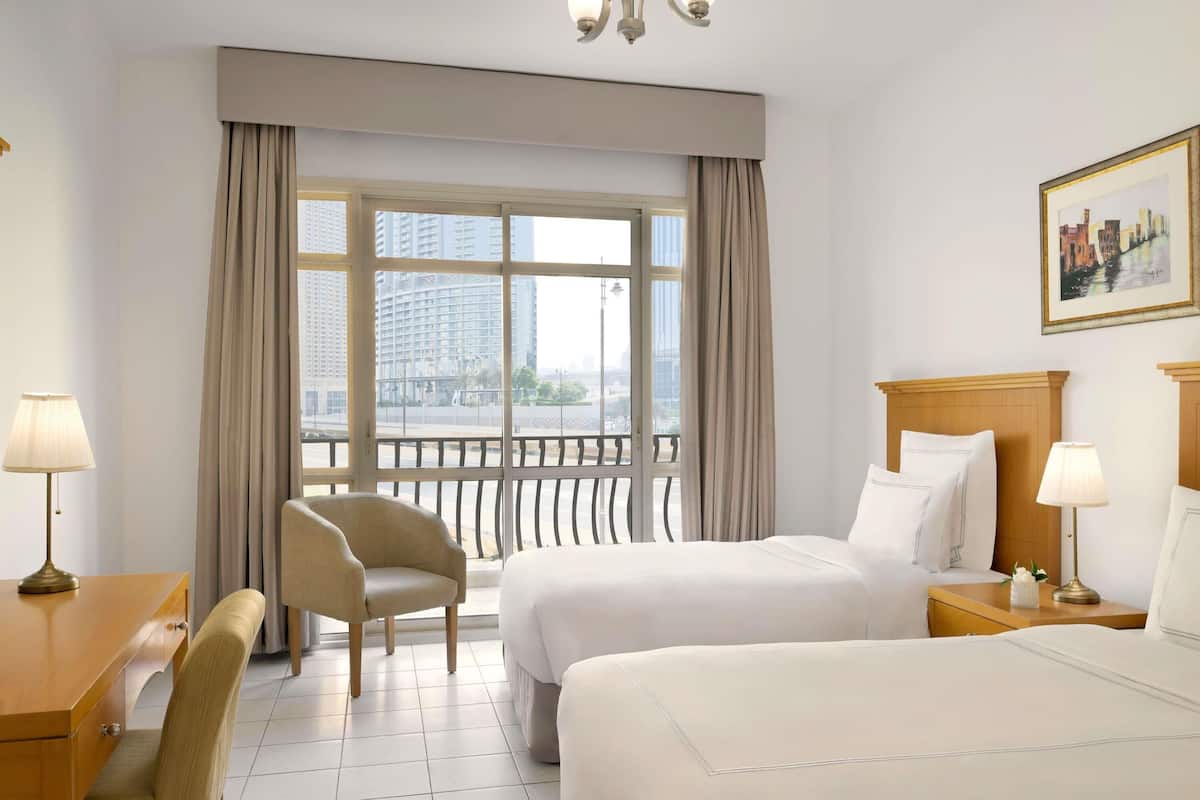 A hotel room with two beds, a desk, a chair, and a large window with curtains.