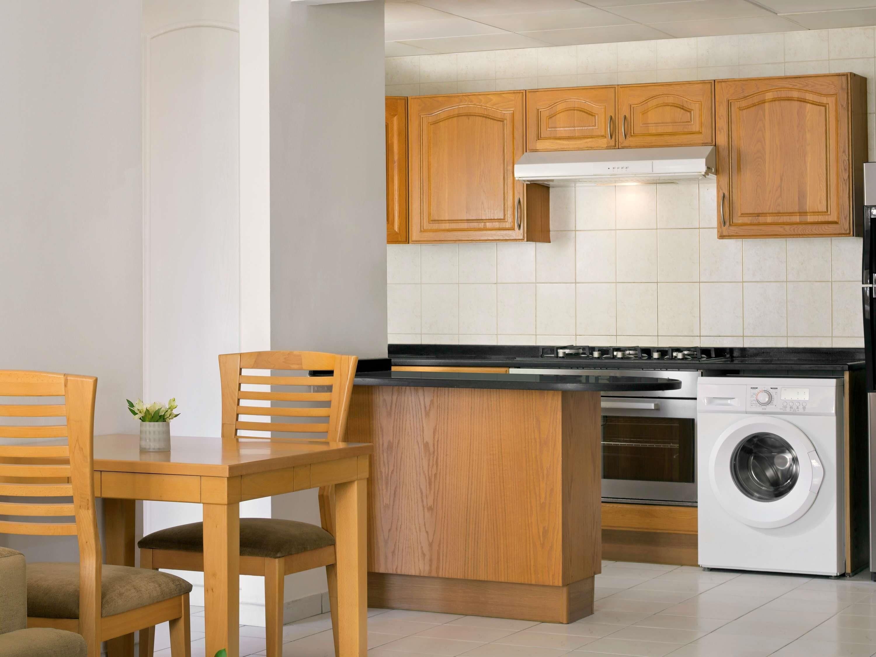 A kitchen with wooden cabinets, a stove, a washing machine, and a dining area with chairs and a table.