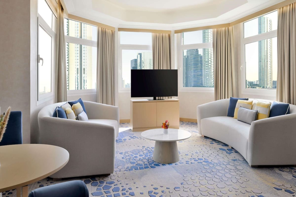 A hotel room with two sofas, a TV, a coffee table, and large windows with city views.