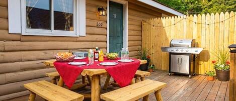 A wooden cabin with a deck, picnic tables, a grill, and a door marked with the number 202.