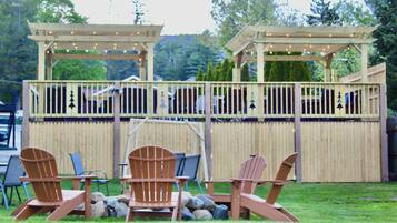 An outdoor seating area with wooden chairs and tables, a wooden pergola with string lights, and a wooden fence.